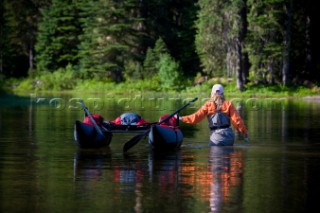 A flyfisherwoman, Doreen Harper, wades her pontoon boat away from the shoreline of a small lake in the Cascade Mts. of Washington State.