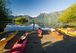 Ben Sanders walks past a group of kayaks while holding a paddle in Lago Yelcho, Chile.