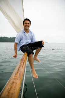 Man smiling on bowsprit of sailboat, Casco Bay, Maine, New England. (releasecode: rausher and rausherPR)