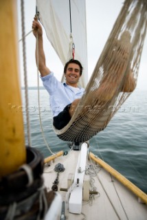 Man smiling in a hammock while cruising on sailboat, Casco Bay, Maine, New England. (releasecode: rausher and rausherPR)