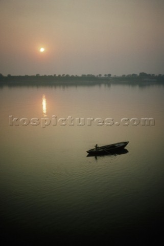 A boy gently guides a rowboat at dawn on the Ganges river near Varanasi
