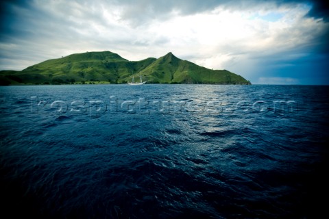 A white boat sailing on the dark blue waters of the Flores Sea sails buy one of the lush tropical is