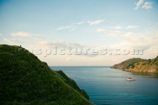 A man sits on the lush green grass covered hillside overlooking his boat in the bay of a small island in the Nusa Tenggara region in Indonesia.
