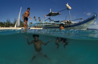 Filipino boys swim from off an outrigger boat anchored on shore. Boracay Philippines.