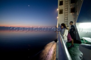 On the deck of a trans-Adriatic car ferry crossing an adventurous travelers watches the sunrise over calm seas.