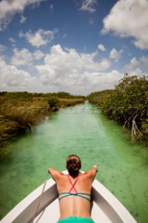 A young woman in a bikini sits in the bow of a white boat as it moves through teal-green water of the Sian Kaan Preserve. David Hanson/Aurora Photos/Kos Pictures
